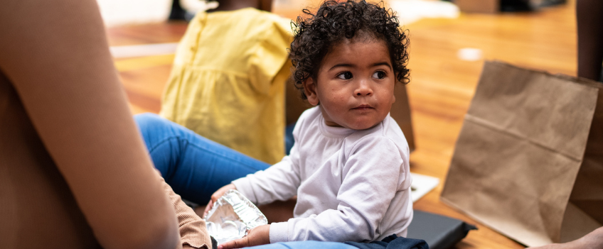 Baby sitting on floor with mother in shelter.